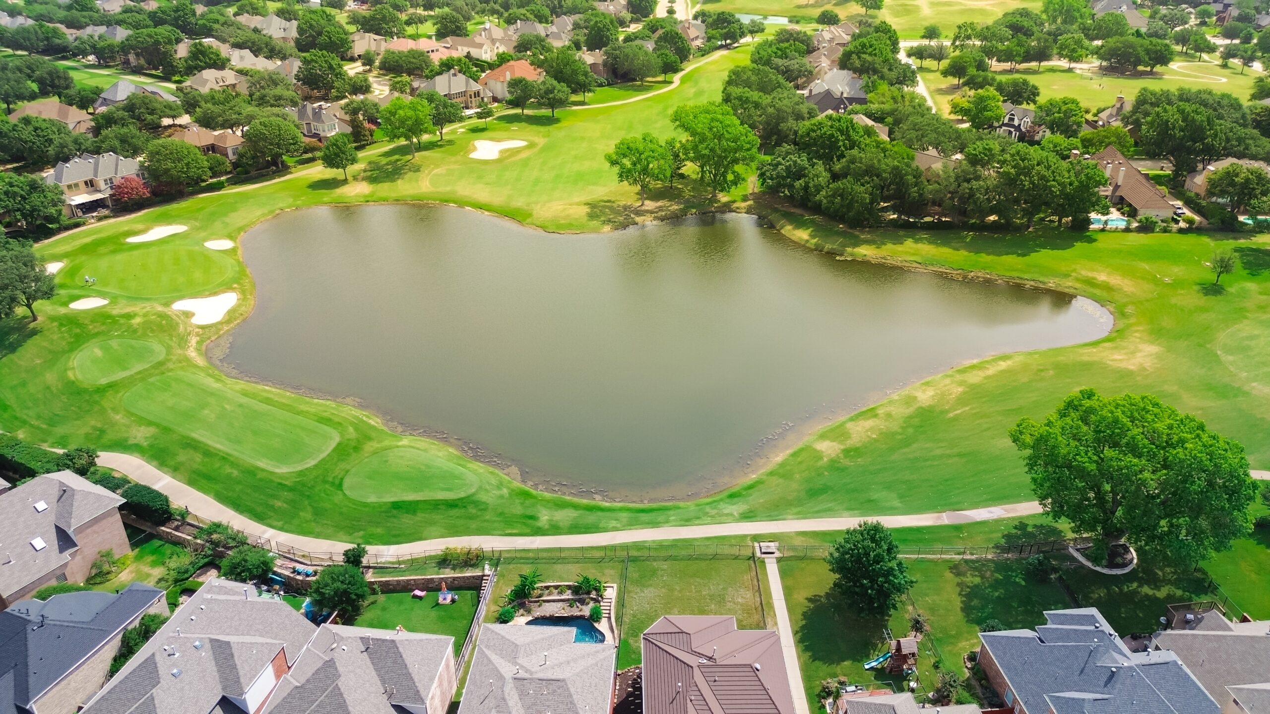 A picturesque neighborhood golf course and pond in Plano, Texas, surrounded by green and weed-free lawns.