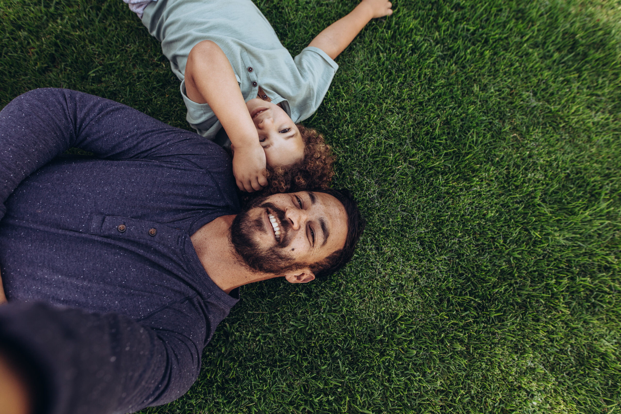 Father and child laying on a thick, lush green lawn after professional lawn fertilizer treatment