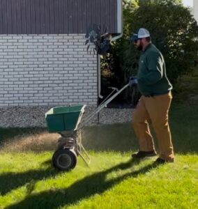 Certified technician spreading seed for fall overseeding on a healthy, weed-free green lawn.