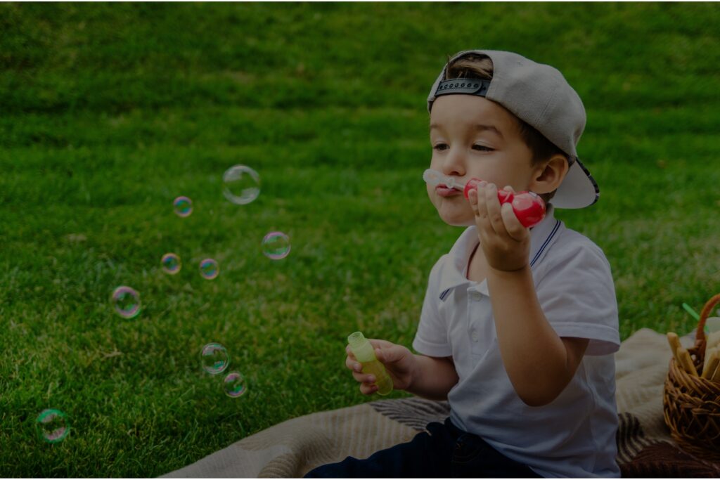 Boy blowing bubbles on a vibrant green and weed-free lawn.