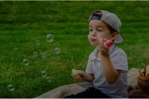 Boy blowing bubbles on a vibrant green and weed-free lawn.