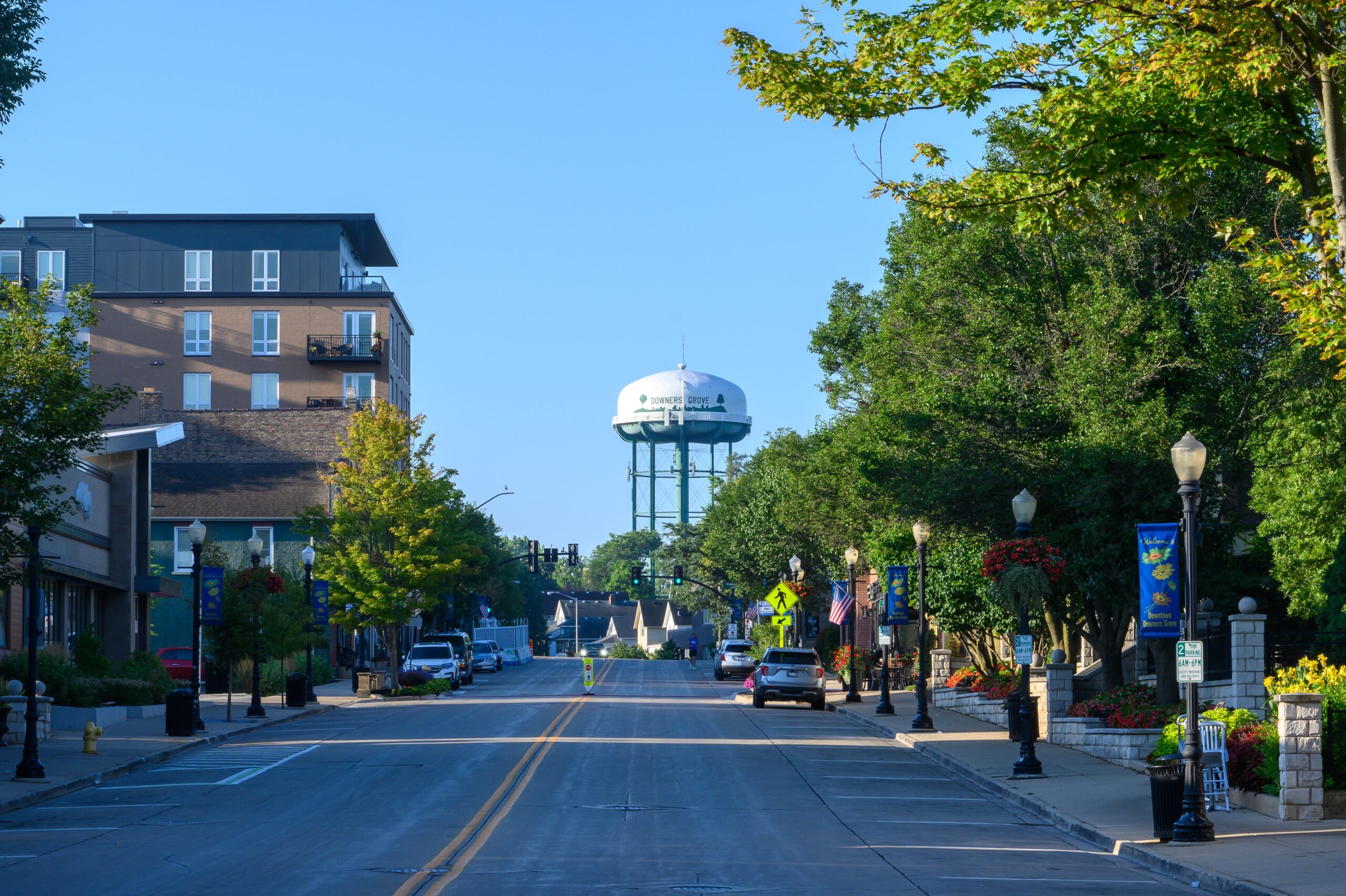 View looking south down Main Street in Downers Grove, Illinois, with the iconic Downers Grove water tower visible on a clear summer morning.
