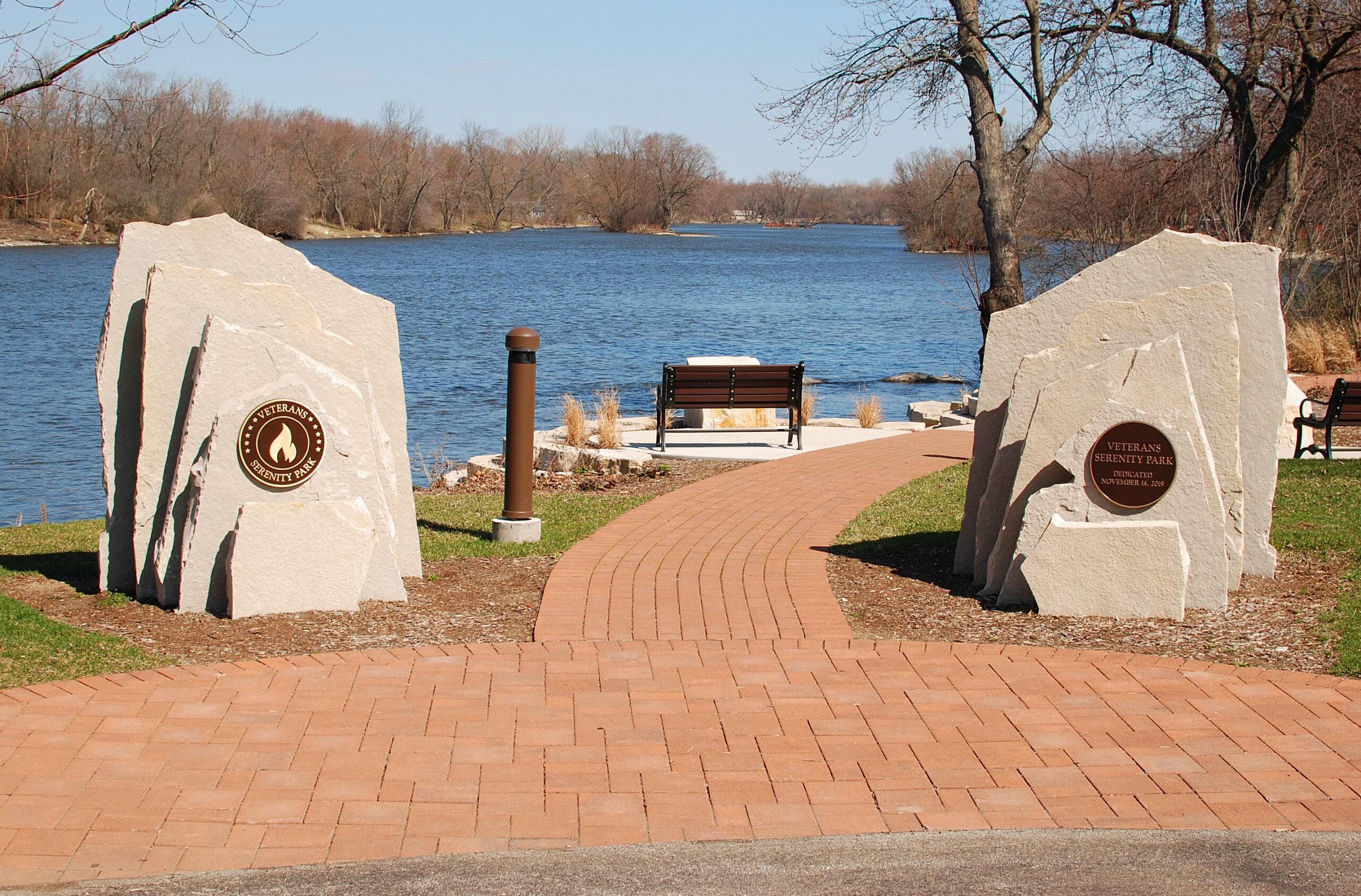 Stone markers at the entrance to Veterans Serenity Park in Oswego, Illinois, surrounded by a well-maintained green lawn.