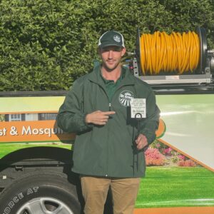 Lawn care company technician from Dr. Green Services standing beside service truck and company flag