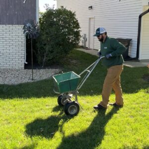 Technician applying seed with lawn spreader during fall aeration and seeding service
