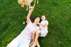 Mother and child lying on a green lawn with their dog enjoying pet safe lawn care.