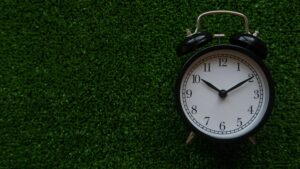 Alarm clock on green grass representing lawn care timing for seasonal lawn treatments